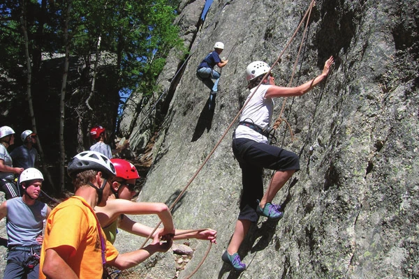 A top roping group at the base of a crag, with an instructor coaching a belayer while a climber moves up the route