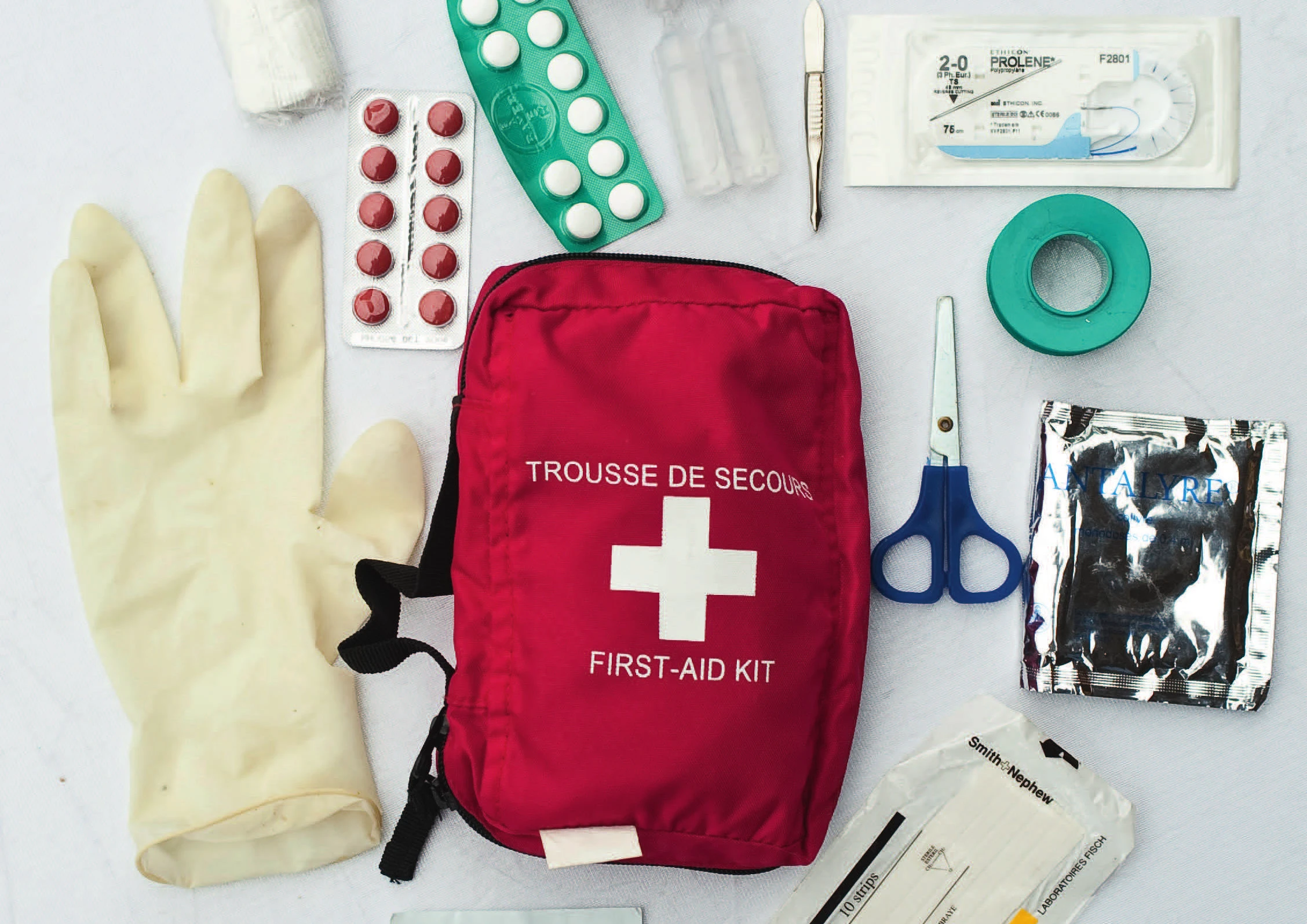 A climbing first aid kit laid open, with gloves, medication, tape, scissors, sutures, and a scalpel