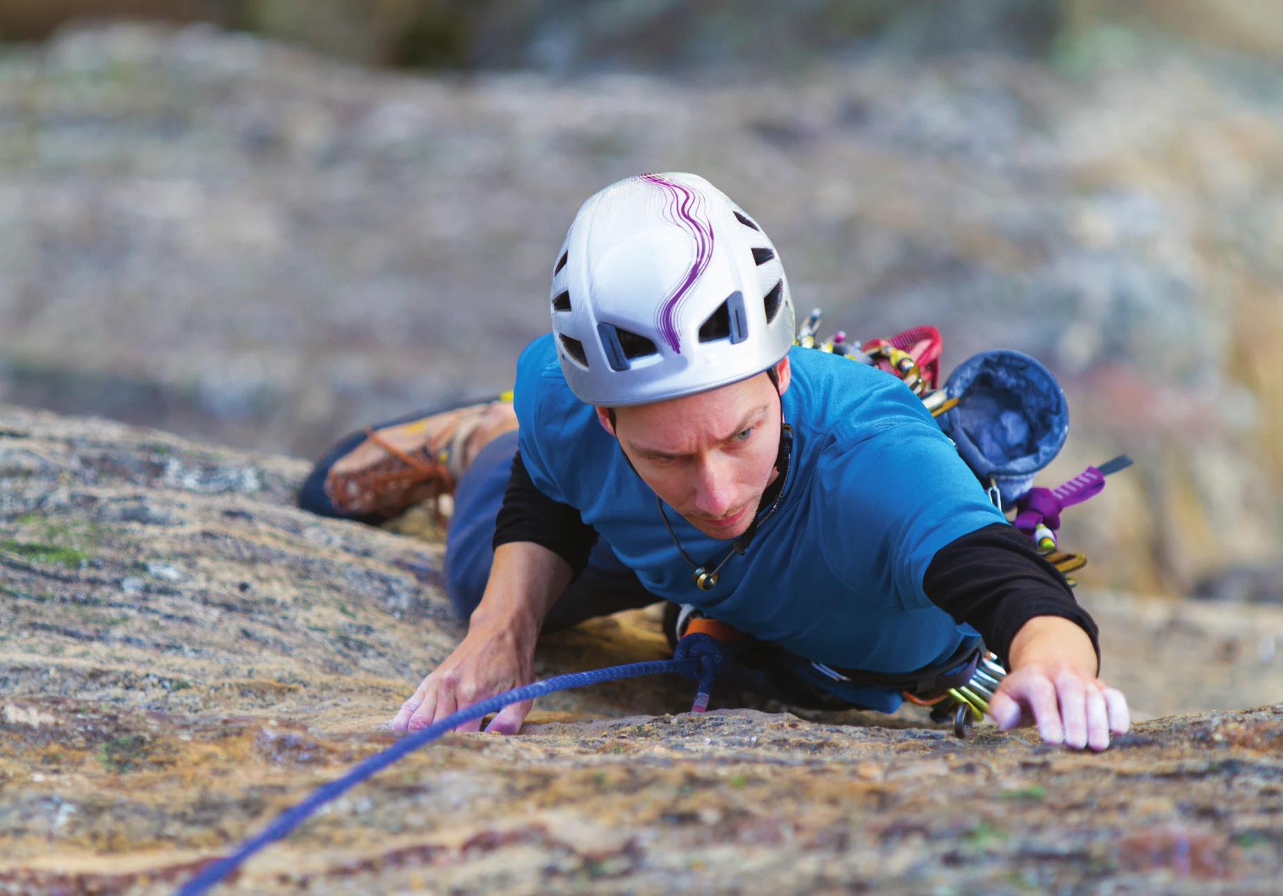 A climber in a white helmet reaching for a hold on a featured face