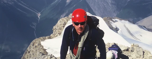 A climber wearing a red climbing helmet on a snowy ridge